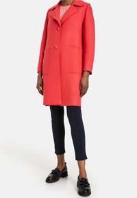 Coral wool blend coat with a notched collar, two front pockets, and a straight cut. Paired with navy slim-fit trousers and black shoes.