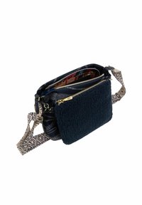 Sac bandoulière en tissu bleu marine avec une pièce en polaire texturée, une sangle à motifs et des accents en métal doré. Plusieurs compartiments visibles à l'intérieur.