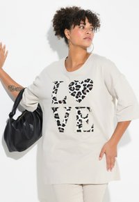 Beige T-Shirt mit großem "LOVE"-Aufdruck in Leopardenmuster. Das Shirt hat einen runden Ausschnitt und Dreiviertelärmel.