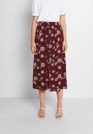 Mujer que lleva una blusa blanca de manga corta con una falda midi roja de cintura alta con estampados florales blancos y botones delanteros.