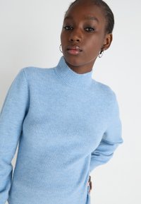 Svetlo modra, rebrasta pulover s turtleneck ovratnikom in dolgimi rokavi. Mehka tekstura in prilegajoč oblikovanje, zasnovano za tesno prileganje na telo.