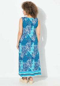 Robe maxi aux motifs bleus avec des motifs géométriques et floraux, sans manches, et un ourlet rayé. Le matériau a une texture lisse.
