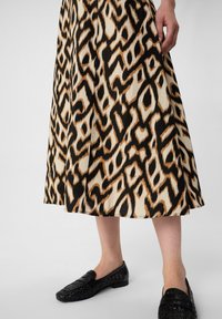 Langes Rock mit einem Schwarz-, Beige- und Braunfarbenen Leopardenmuster. Getragen mit schwarzen, gewebten Loafers, die eine glatte Stofftextur hervorheben.