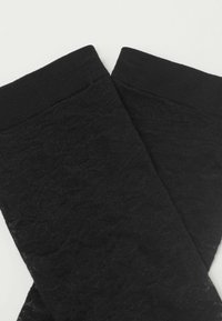 Černé texturované podkolenky s listovým vzorem a hladkým elastickým lemem nahoře. Materiál působí měkce a je složitě tkaný.