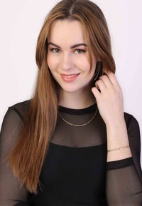 Gold chain necklace and bracelet on a person wearing a black mesh long-sleeve top. Hair is straight and down, framing the face.