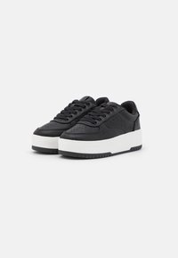 Zwarte leren sneakers met een dikke witte rubberen zool, ronde neus en platte zwarte veters. Voorzien van ventilatiegaten op de neus.