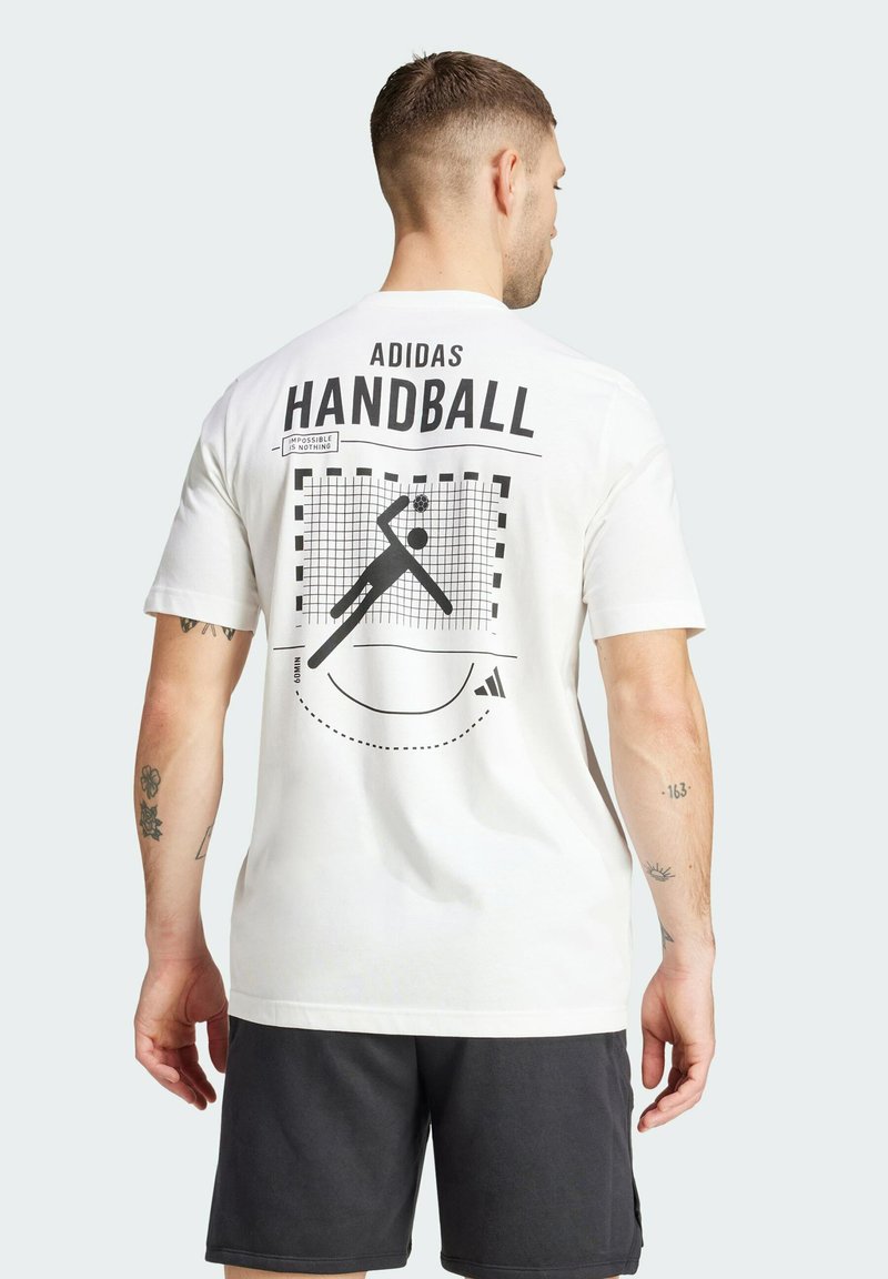 Camiseta blanca de algodón con un gráfico de un jugador de balonmano en la parte posterior, con texto y acentos en negro, cuello redondo y mangas cortas.