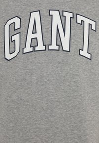 Felpa grigia con una grande grafica bianca con la scritta "GANT" contornata di blu. Tessuto morbido e design casual.