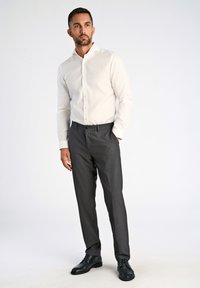 Camicia bianca con bottoni abbinata a pantaloni grigi scuri su misura e scarpe in pelle nere. Tessuto liscio con un design aderente. Sfondo semplice.
