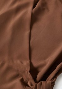 Gros plan d'un tissu marron lisse avec une couture visible et un détail froncé sur un côté.