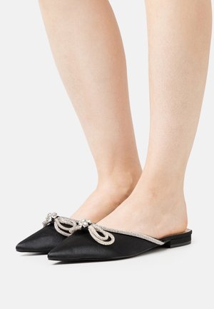 Mules en satin noir à bouts pointus, ornées d'un nœud bijou et d'une bordure en strass. Modèle à enfiler avec un petit talon.