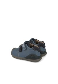 Zapatos infantiles azules con acabado mate, que cuentan con correas de Velcro, puntera redondeada y suelas de goma texturizadas. Acentos cosidos en azul más oscuro.
