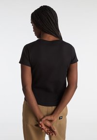 Zwart T-shirt met korte mouwen en een klassieke ronde halslijn. Eenvoudig, aansluitend ontwerp dat boven de taille valt, gemaakt van een soepele, rekbare stof.