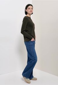 Long-sleeve, olive green top paired with blue wide-leg jeans. The outfit features a relaxed fit, smooth texture, and minimalistic design.