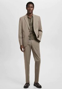 Beige tailored suit with a single-button blazer, paired with a textured olive-green knit polo. Complete with dark brown shoes.