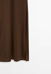 Jupe en tissu marron avec un ourlet droit et une fente latérale, montrée suspendue sur un fond blanc uni.