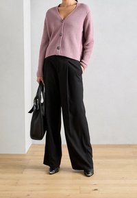 Jasnoróżowy kardigan o prążkowanej fakturze z czterema guzikami, zestawiony z czarnymi spodniami o szerokich nogawkach i wysokim stanem. W zestawie czarna torebka oraz błyszczące buty.
