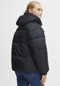 Svart boblejakke med hette, med kviltet design, blank overflate og elastiske mansjetter. Brukt sammen med blå jeans.