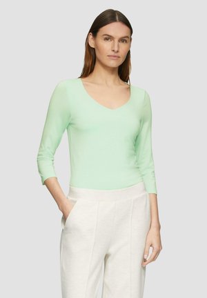 Mintgroene lange mouwen top met V-hals en een zachte textuur, gecombineerd met crèmekleurige, hoog-waist broek met zijzakken.
