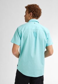 Korte mouwen shirt van lichtturquoise stof, met een standaard kraag en een rugpaneel met een knoopdetail. Getailleerde pasvorm met afgeronde zoom.