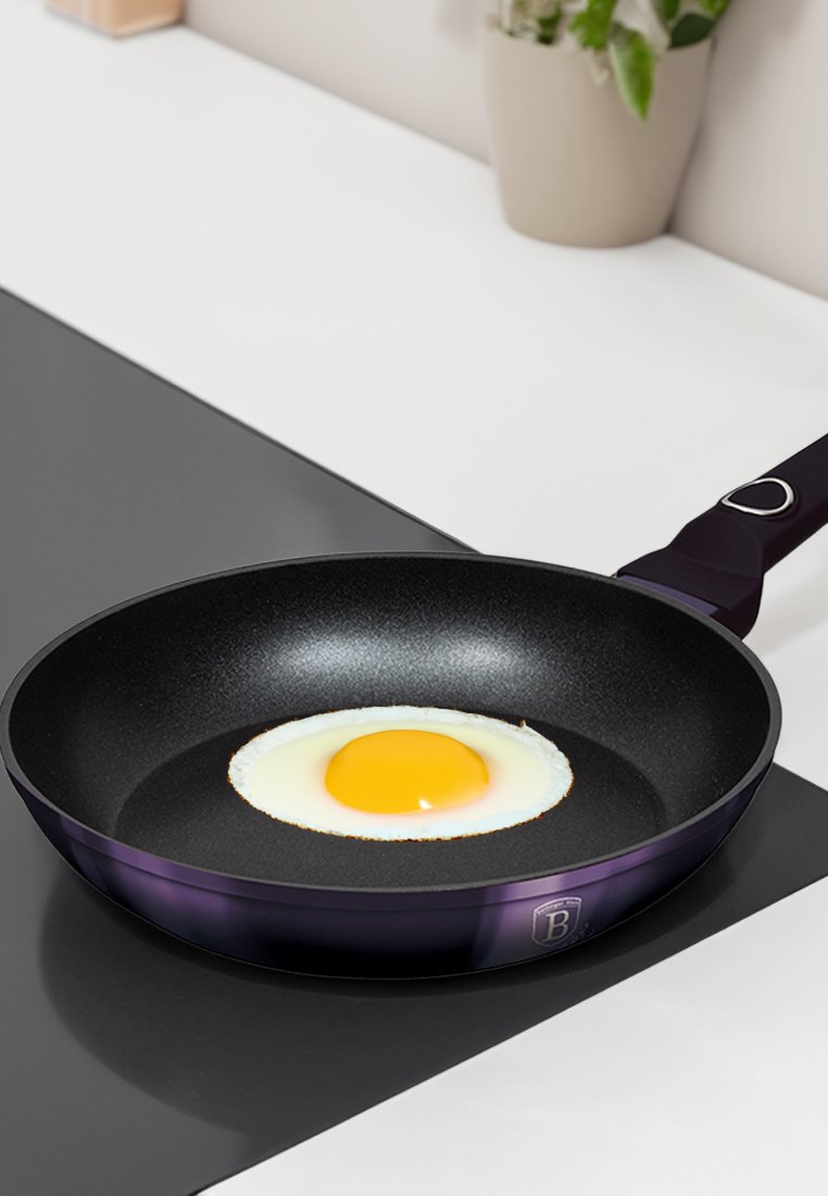 Zwarte koekenpan met een paarse rand, met een gebakken ei in het midden. Glad antiaanbakoppervlak op een zwart keukenblad.