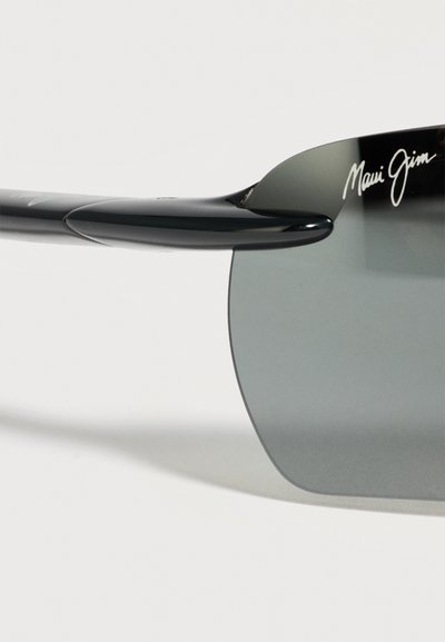 Γυαλιά ηλίου Maui Jim με μαύρο περίγραμμα, σκουρασμένους φακούς και ημι-χωρίς πλαίσιο σχέδιο, με το όνομα της μάρκας στην γωνία του φακού.
