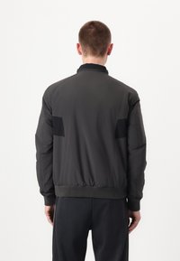 Giubbotto bomber da uomo in grigio scuro, con orlo e polsini a costine, tessuto liscio e pannelli neri a contrasto sulla schiena.