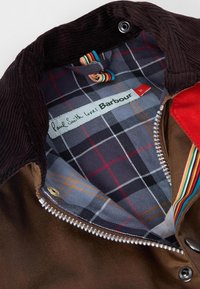 Brown corduroy collar with a zip, featuring a multi-colored striped inner label. Inside: plaid lining in blue, gray, and red patterns.