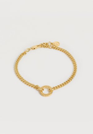 Βραχιόλι με χρυσή αλυσίδα και κρεμαστό κυκλικό δαχτυλίδι με χαραγμένο κείμενο και μια μικρή ετικέτα κοντά στο κούμπωμα, εμφανίζεται σε λευκό φόντο.