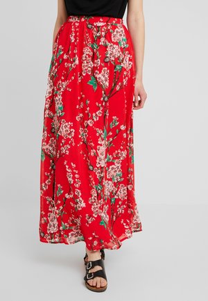 Jupe longue rouge à fleurs avec une coupe ample, présentant des motifs de fleurs blanches et vertes, une taille froncée et un tissu léger et fluide.
