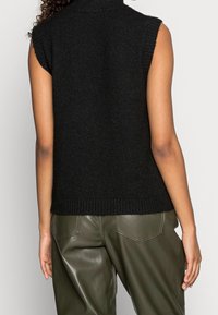 Top nero senza maniche in maglia con colletto alto, caratterizzato da un orlo a coste. Abbinato a pantaloni in pelle verde testurizzata.