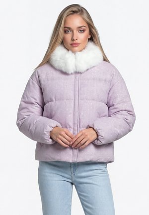 Junge Frau mit langen blonden Haaren, die eine hellviolette Steppjacke mit weißem Kunstpelzkragen und hellblaue Jeans trägt, steht still.