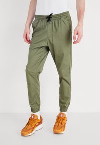 Khaki joggerbyxor med elastisk midja, dragsko och smalnande ärmslut. Tillverkade av lättviktsmaterial och med sidofickor.