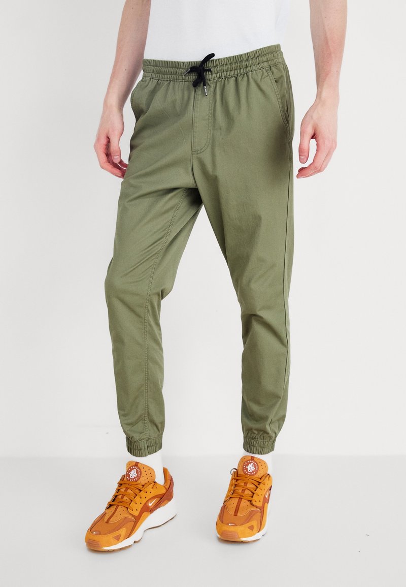 Khaki joggerbyxor med elastisk midja, dragsko och smalnande ärmslut. Tillverkade av lättviktsmaterial och med sidofickor.