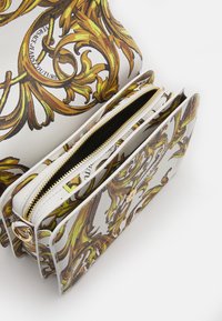 Vit zip-försedd väska med gyllene och bruna utsmyckade barockmönster. Flera fack med en slät yta och gyllene hårdvarudetaljer.