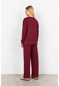 Burgundy loungewear-setti, joka sisältää väljät pitkähihaiset paidan ja leveät housut, valmistettu pehmeästä, tekstuurista kankaasta, rentoa siluettia.