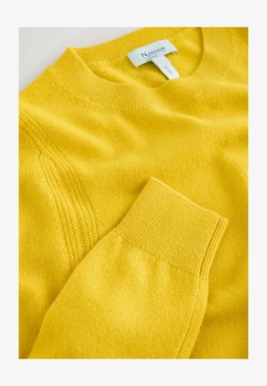 Sárga kötött pulóver, bordázott kerek nyakkivágással és mandzsettával, sima textúrával és finom varrási részletekkel. Címke látható a nyaknál.