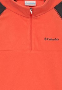 Pull en polaire rouge avec un zip quart sur le devant, des accents noirs sur les épaules et un logo Columbia brodé sur la poitrine gauche.