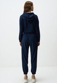 Survêtement bleu marine avec capuche, doté de poignets élastiques, de poches latérales et d'une coupe décontractée. Texture lisse et tissu léger.