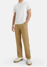 T-shirt blanc à manches courtes, pantalon beige à jambes droites et baskets de couleur claire. Le pantalon comporte des poches avant et des passants pour ceinture.