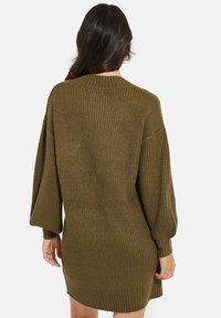 Olivgrünes Strickkleid mit gerippter Textur, übergroßen Ärmeln und Rundhalsausschnitt, das hinten oberhalb des Knies endet.