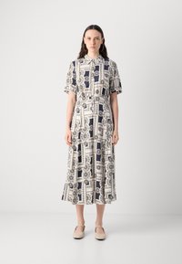 Short-sleeve, button-up dress featuring a navy and white geometric pattern, cinched waist, and a flared hem. Model wearing soft beige footwear.