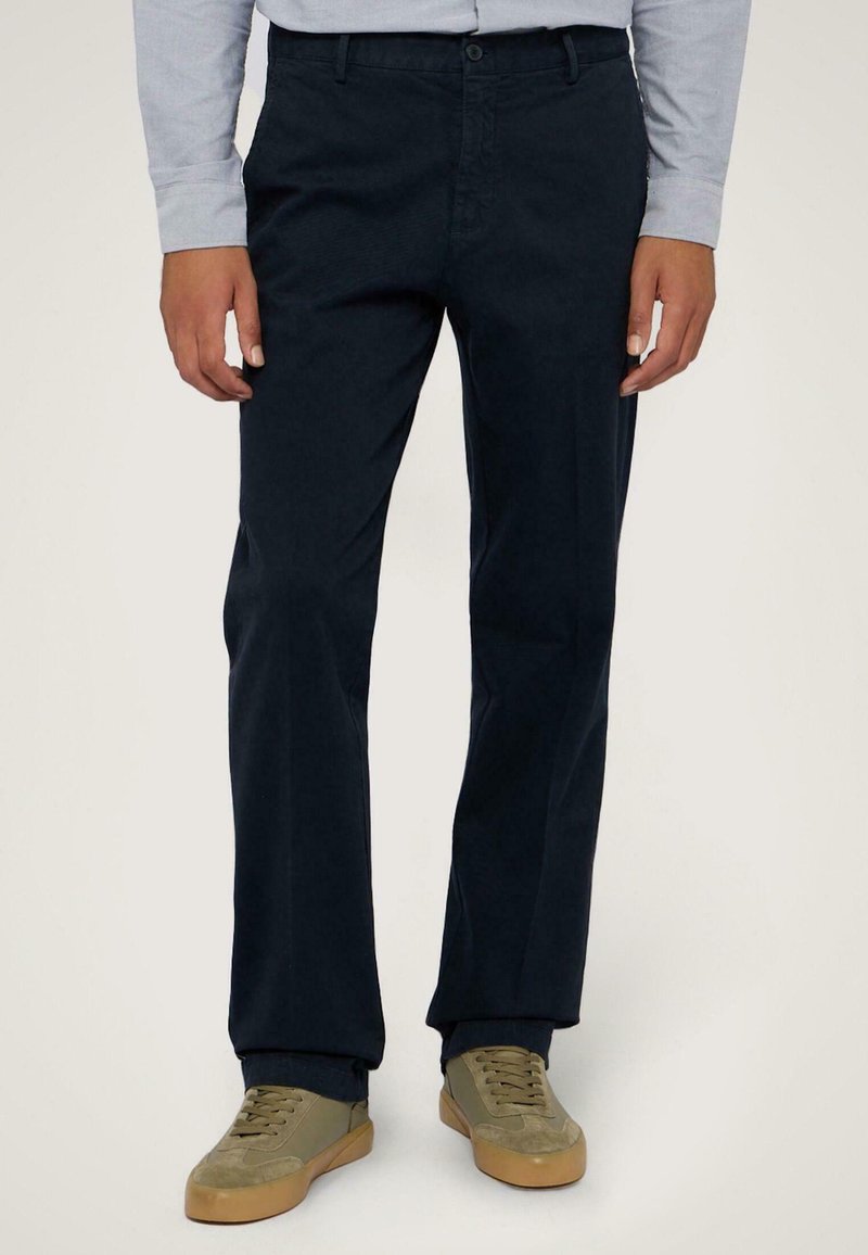 Chino blu navy realizzati in misto cotone, caratterizzati da un design a gamba dritta, tasche frontali e zip. Abbinati a sneakers color oliva.