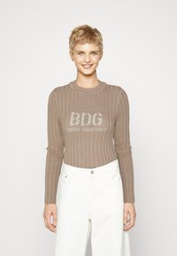 Brun ribbet genser med lange ermer, featuring en rund hals og trykt tekstdesign på forsiden, parret med hvite høytlivsbukser.