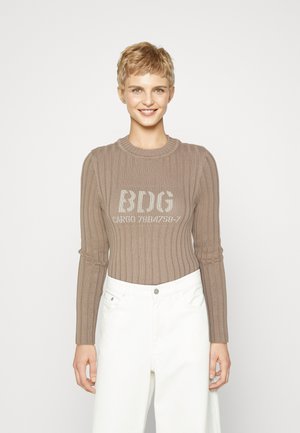 Brun ribbet genser med lange ermer, featuring en rund hals og trykt tekstdesign på forsiden, parret med hvite høytlivsbukser.