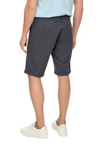 Shorts gris foncé en tissu léger, dotés de deux poches arrière avec boutons, et d'une coupe droite, portés avec des baskets blanches.