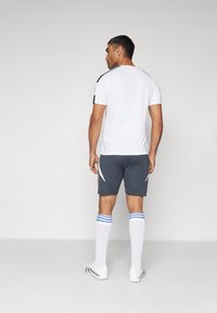 Vitt kortärmat träningsskjorta, grå shorts med vita detaljer, vita strumpor med blå ränder och vita sportskor.