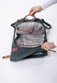 Zaino in pelle verde con dettagli marroni, chiusura a cerniera e interno a quadretti grigi. Presenta più scomparti e un esterno texturizzato.