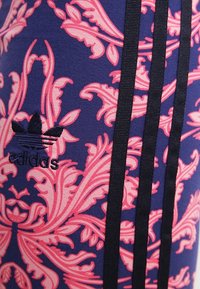 Legíny s námořnickým pozadím a růžovým květinovým vzorem, černými vertikálními pruhy a vyraženým černým logem Adidas.