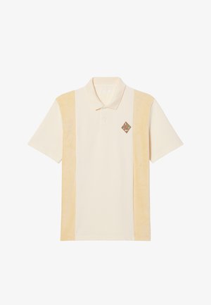 Polo shirt in cream with two side panels in soft, pale yellow. Features a small embroidered diamond logo in brown and green on the chest.